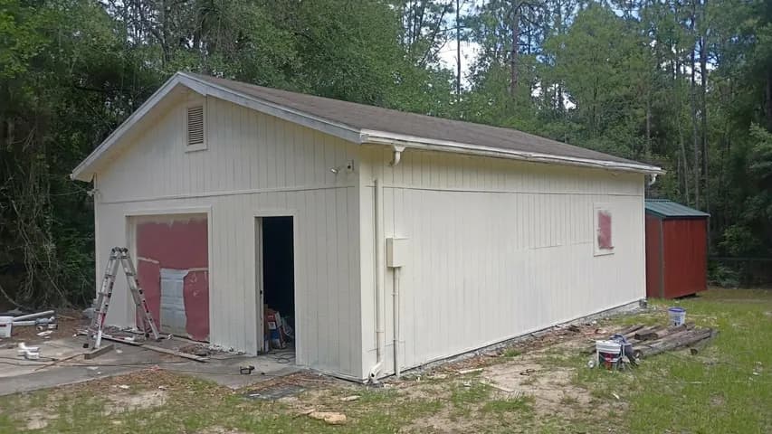 Detached garage mid-project — siding patched and primed, ladder up