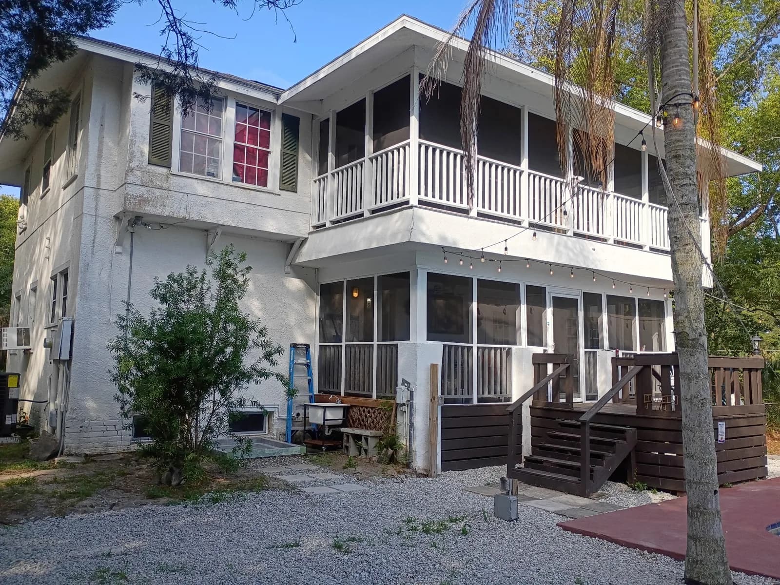 Two-story home rear before — screened porch, deck stairs, gravel yard