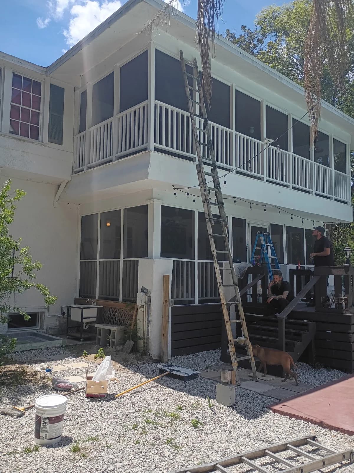 Two-story home rear during work — crew on ladders painting upper story