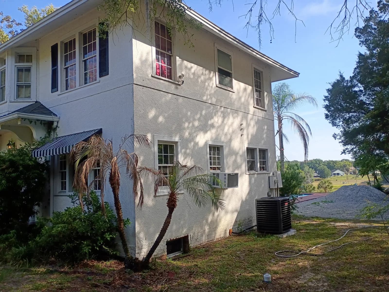Two-story home side exterior before — multiple windows and palm trees