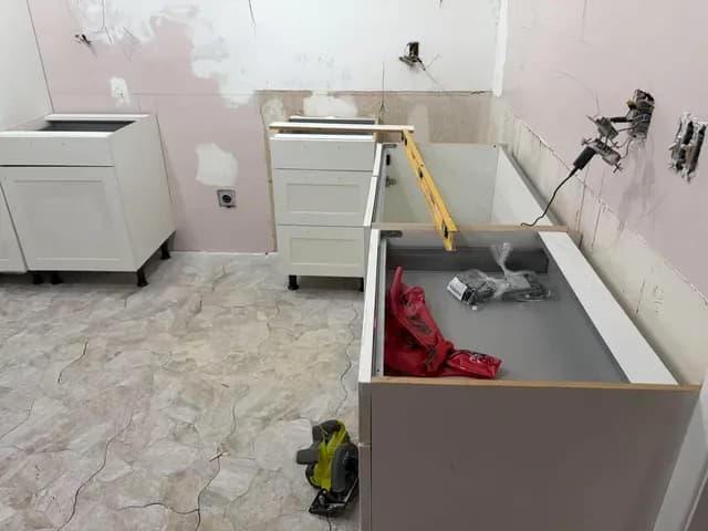 White shaker base cabinets being set over a new stone-look tile floor