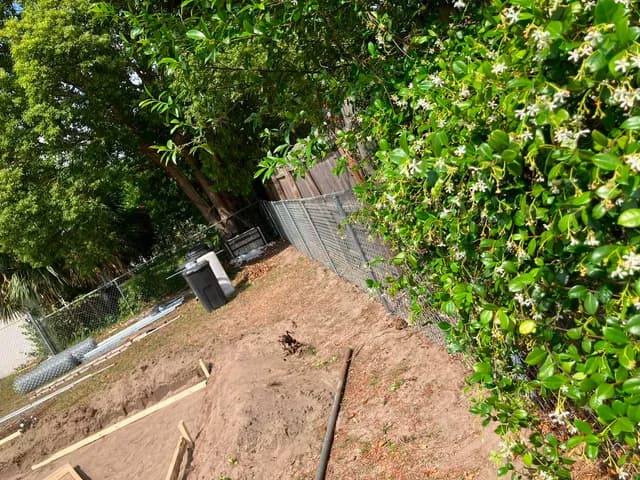 Concrete footer formed and prepped along a backyard fence line