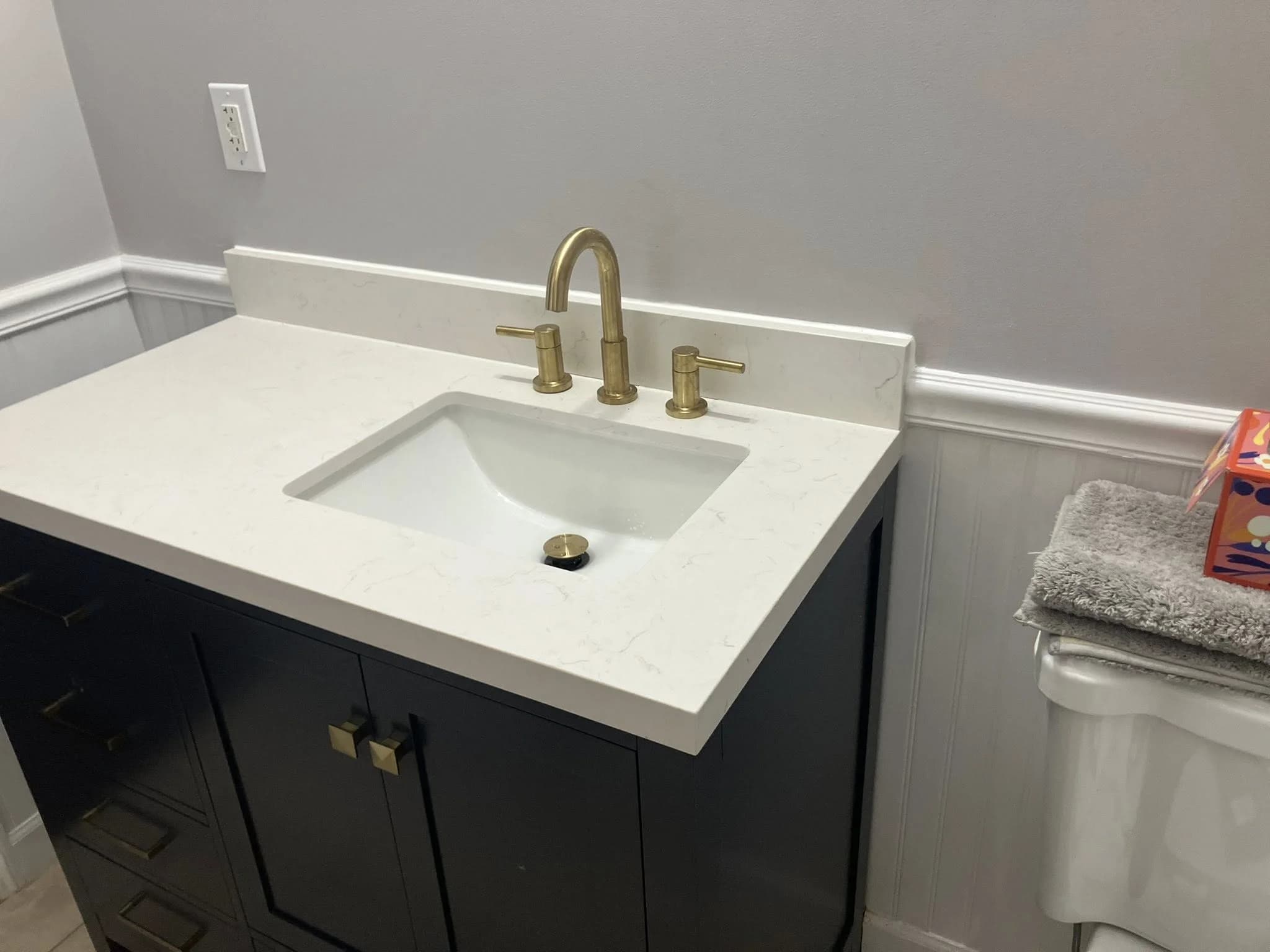 White quartz bathroom vanity with gold fixtures and frameless mirror