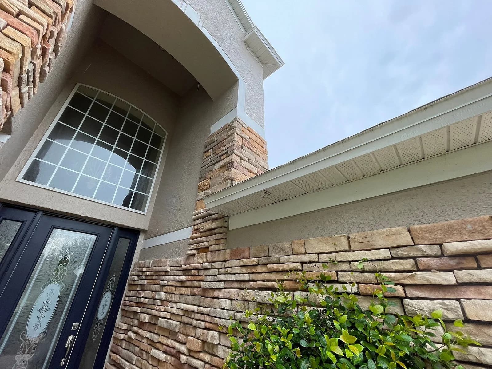 Exterior stone veneer column and arch accent work with navy entry door